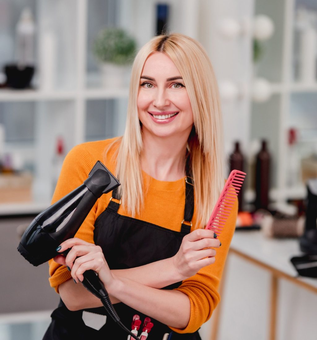 beautiful-blond-girl-hairdresser-looking-camera-smiling-holding-hair-dryer-beauty-salon